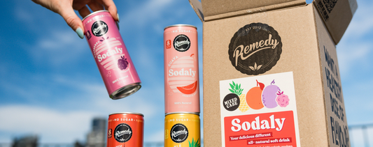 Picture of cans of Sodaly outside, next to a box with the Remedy Drinks and Sodaly logos.