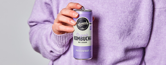 Person in purple jumper holding Remedy Passionfruit Kombucha