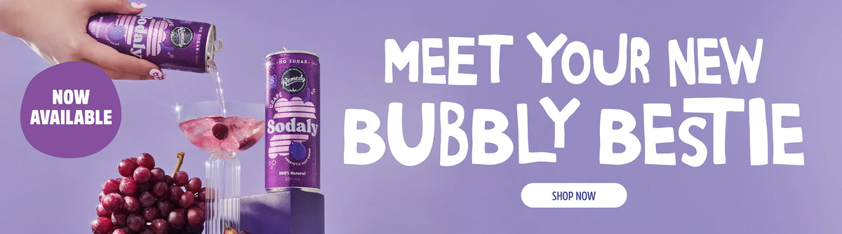 A promotional banner for Sodaly sparkling drink, showing a hand pouring purple liquid from a can into a glass, with a second can, grapes, and large text reading 'MEET YOUR NEW BUBBLY BESTIE' on a purple background.